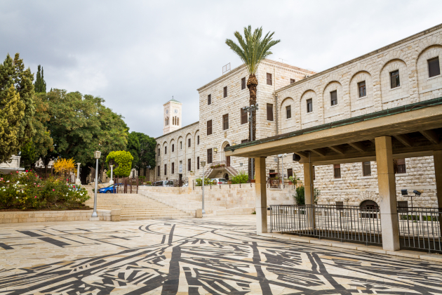Historisches Klostergebäude mit Glockenturm und exotischer Vegetation, gepflasterter Innenhof mit schwarzem Muster, in Nazareth, Israel.