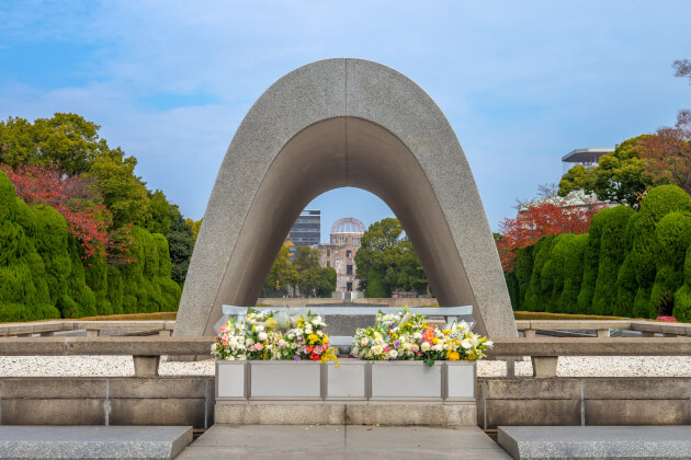 Cenotaph im Hiroshima Peace Memorial Park mit Blick auf die Atombombenkuppel. < Gebeco