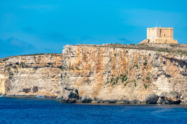 Historischer Santa Maria Tower auf Comino über steiler Kalksteinküste mit Blick auf das Mittelmeer bei klarem Himmel. | Gebeco
