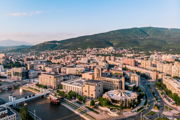 Skopje Nordmazedonien – Stadtansicht mit Fluss Vardar und modernen Gebäuden vor Bergkulisse