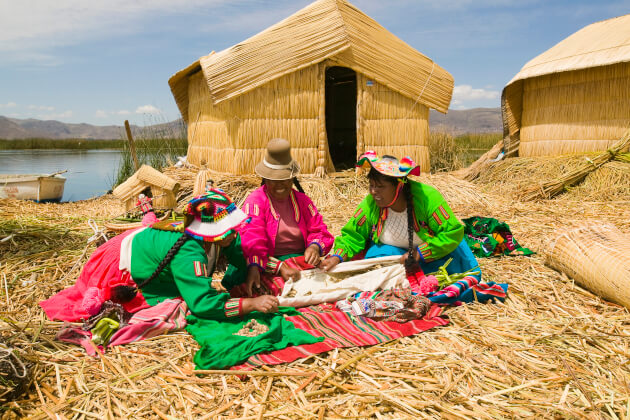 Drei Frauen in traditioneller Kleidung bei Handarbeiten auf einer Schilfinsel der Uros im Titicacasee, Peru. | Gebeco