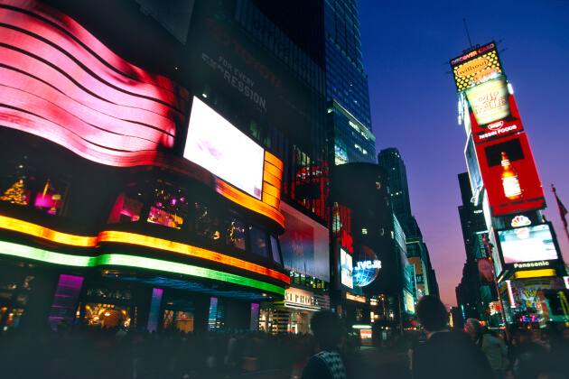 Leuchtende Reklametafeln am Times Square in Manhattan, New York City bei Nacht mit Passanten im Vordergrund. | Gebeco