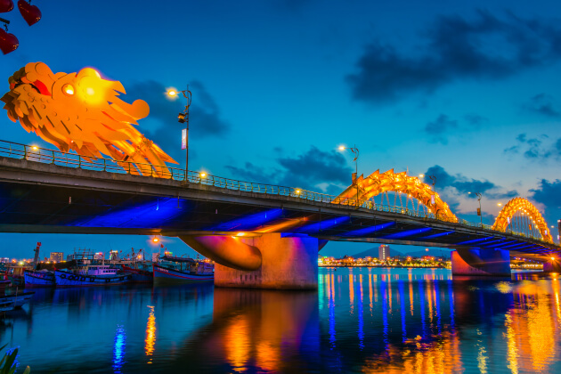 Die berühmte Drachenbrücke von Da Nang bei Nacht, hell erleuchtet in Gold- und Blautönen. | Gebeco