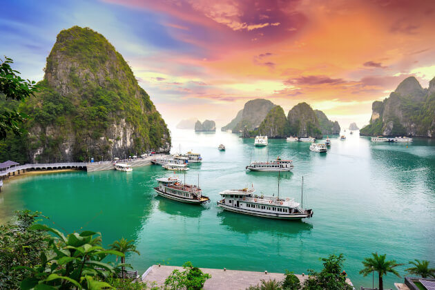 Boote in der Halong-Bucht, umgeben von Karstfelsen bei farbenprächtigem Sonnenuntergang. | Gebeco