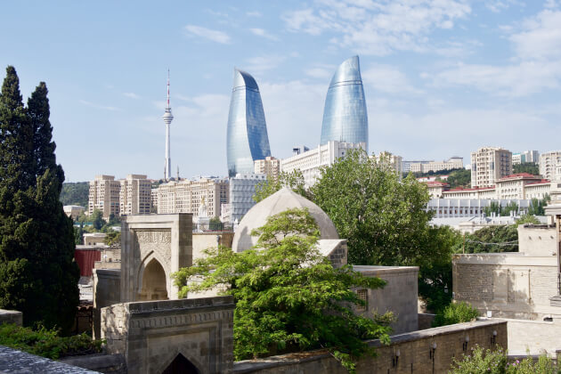 Skyline von Baku in Aserbaidschan mit den berühmten Flame Towers und Fernsehturm, im Vordergrund historische Altstadt mit traditioneller Architektur und Kuppeln.