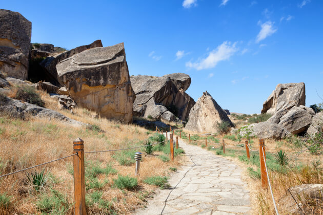 Qobustan Nationalpark in Aserbaidschan mit prähistorischen Felszeichnungen und Petroglyphen, Besucherpfad mit Holzgeländer durch UNESCO-Weltkulturerbe unter blauem Himmel.