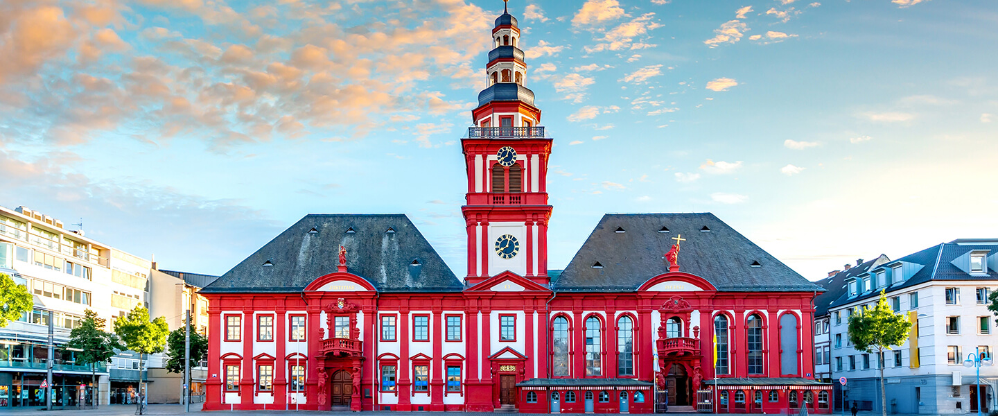 Historisches rotes Rathaus in Mannheim mit Uhrenturm in Deutschland, barocke Architektur auf Marktplatz umgeben von modernen Gebäuden bei Sonnenuntergang.