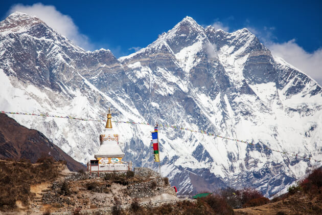 Weiße buddhistische Stupa mit Gebetsfahnen im Vordergrund, im Hintergrund der schneebedeckte Mount Everest. | Gebeco