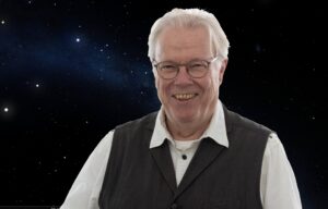 Mann sitzt lächelnd vor einem Sternenhimmel als Hintergrund, Astronom und Experte für Sonnenphysik Dirk Soltau