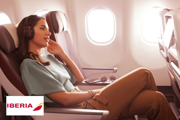 Entspannte Frau in Iberia Business Class mit Kopfhörern, komfortabler Sitz am Flugzeugfenster, warmes Sonnenlicht durchflutet die Kabine, Premium-Flugreise.