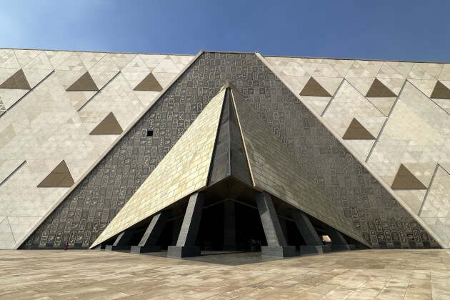 Modernes Museumsgebäude mit pyramidenförmigem Eingang und geometrischen Dreiecksmustern an der Fassade unter blauem Himmel, zeitgenössische Architektur im Nahen Osten.