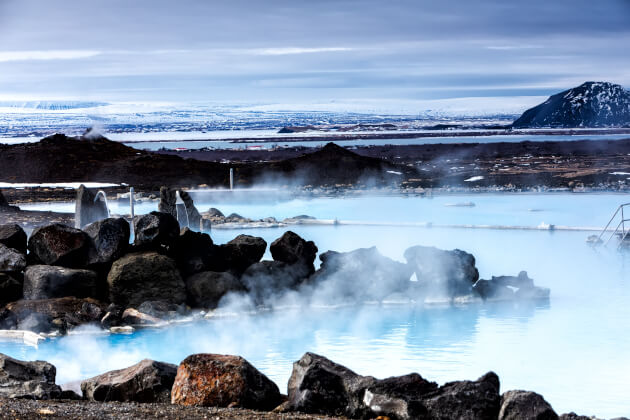 Dampfende, milchig-blaue Thermalquelle in vulkanischer Winterlandschaft mit schwarzem Lavagestein