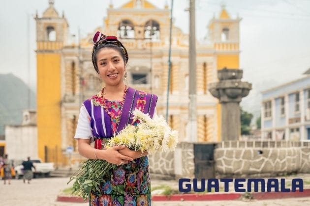 Tradition und Kultur: Guatemaltekische Frau in bunter Tracht vor Kirche in Quetzaltenango mit Blumen Zu den Ländertipps für Guatemala
