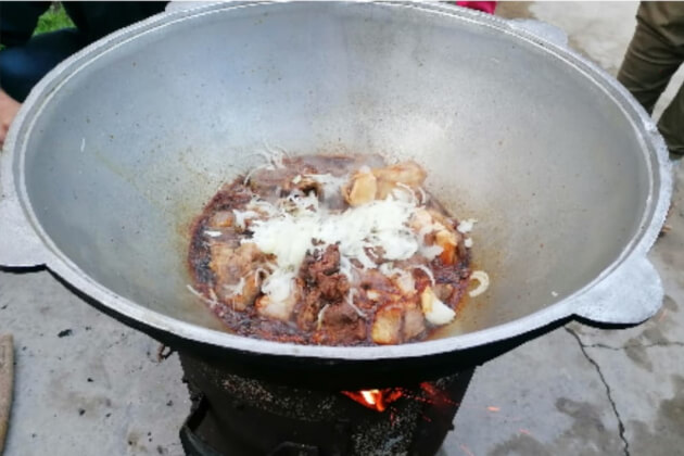 Zwiebeln werden zu den angebratenen Fleischstücken im großen Kazan gegeben und kurz angeschwitzt – zweiter Schritt der Plov-Zubereitung.