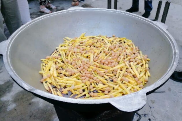 Gelbe Karottenstreifen und Kichererbsen werden im großen Kazan angebraten – dritter Schritt der Plov‑Zubereitung.