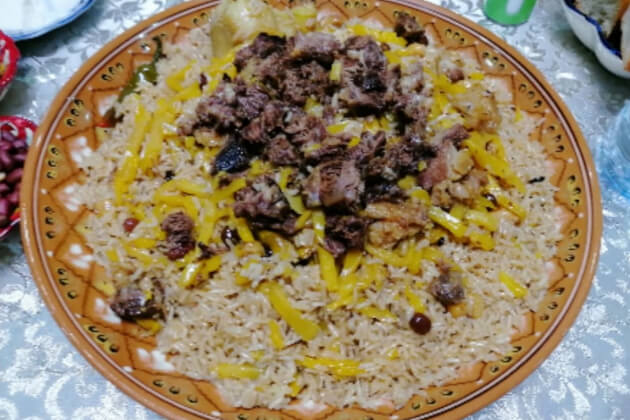 Plov mit Reis, gebratenem Fleisch und gelben Karottenstreifen auf großer Platte zum gemeinsamen Essen.