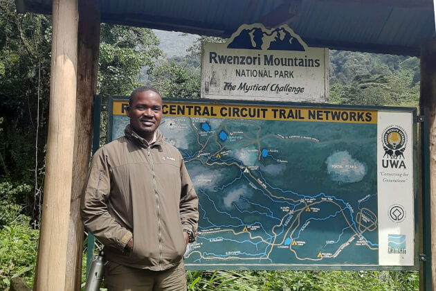Reiseleiter Paul vor Infotafel mit Karte des Rwenzori Mountains National Park (Central Circuit), Uganda