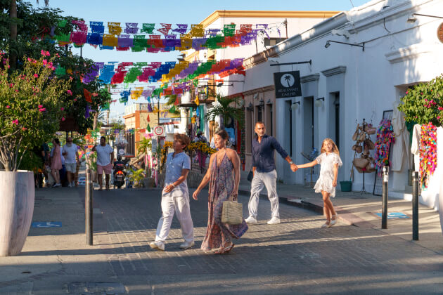 Belebte Altstadt‑Einkaufsstraße mit bunten Papiergirlanden über der Gasse, Passanten und kleinen Läden