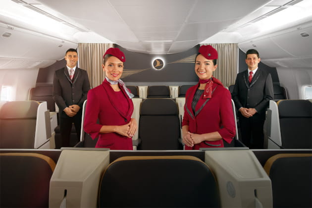 Premium‑Kabine mit Business‑Class‑Sitzen und vier uniformierten Kabinenmitarbeitern; Airline‑Logo an der Wand sichtbar