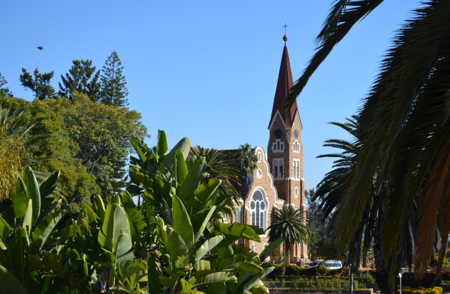Christuskirche Windhoek — rote Backsteinkirche mit spitzem Turm, Palmen im Vordergrund vor klarem blauem Himmel