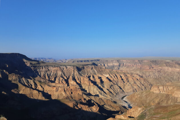 Fish River Canyon, Namibia — weite, erodierte Felslandschaft mit geschwungenem Flusslauf im Schluchtgrund und klarem blauem Himmel