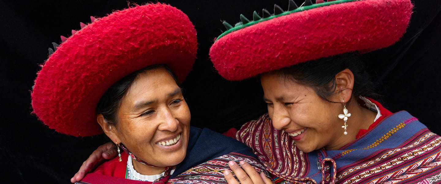 Zwei lachende Frauen in traditioneller Andentracht mit roten Hüten und farbig gewebten Umhängetüchern in Peru